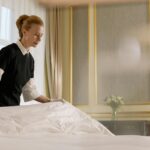 A professional housekeeper fixes a bed in a luxurious hotel room.