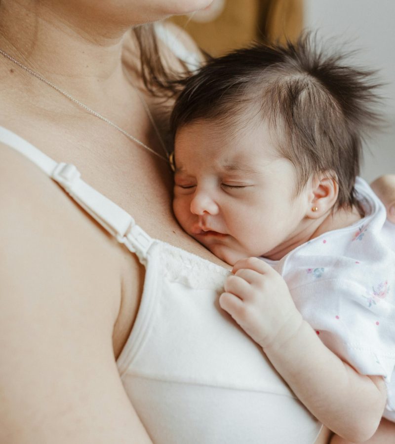 A mother holds her sleeping newborn close, showcasing love and bonding indoors.